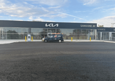 A black van is parked in front of a Kia dealership building with Sansone Jr signage and a service entrance visible.